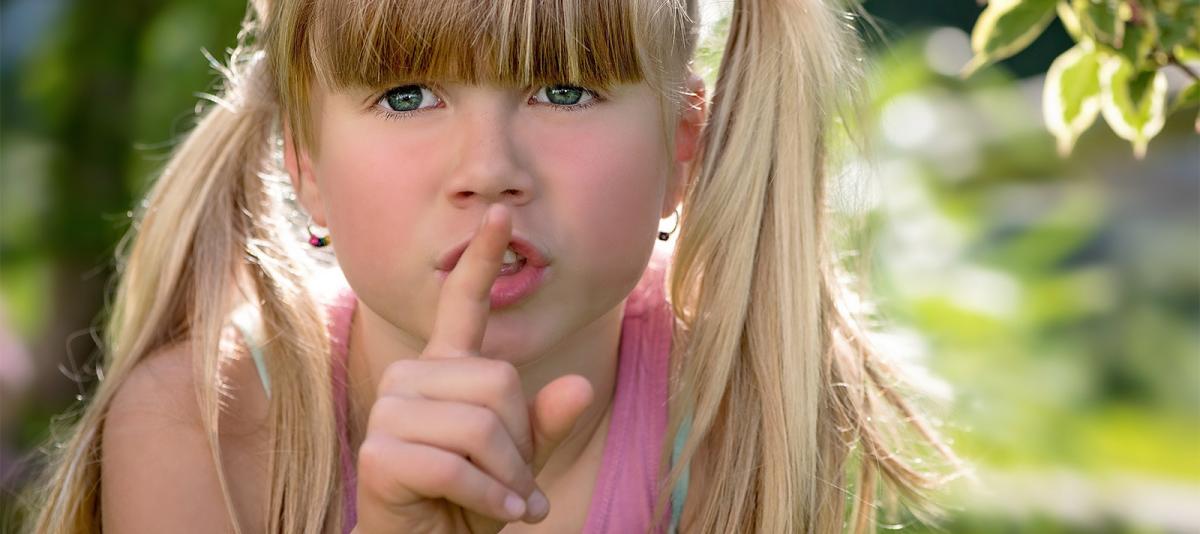 Blonde girl with pony tails with her finger to her lips indicating to be quiet.