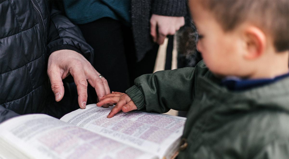 A child pointing to a page of an open bible being held by an adult