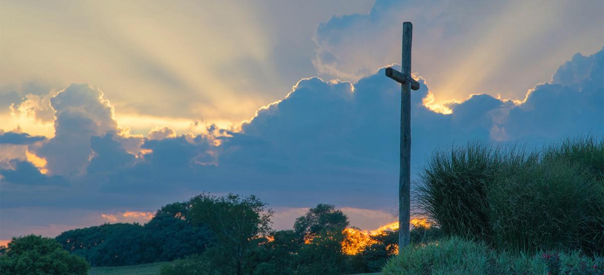 A cross on a green hillside with a beautiful blue sky with puffy clouds