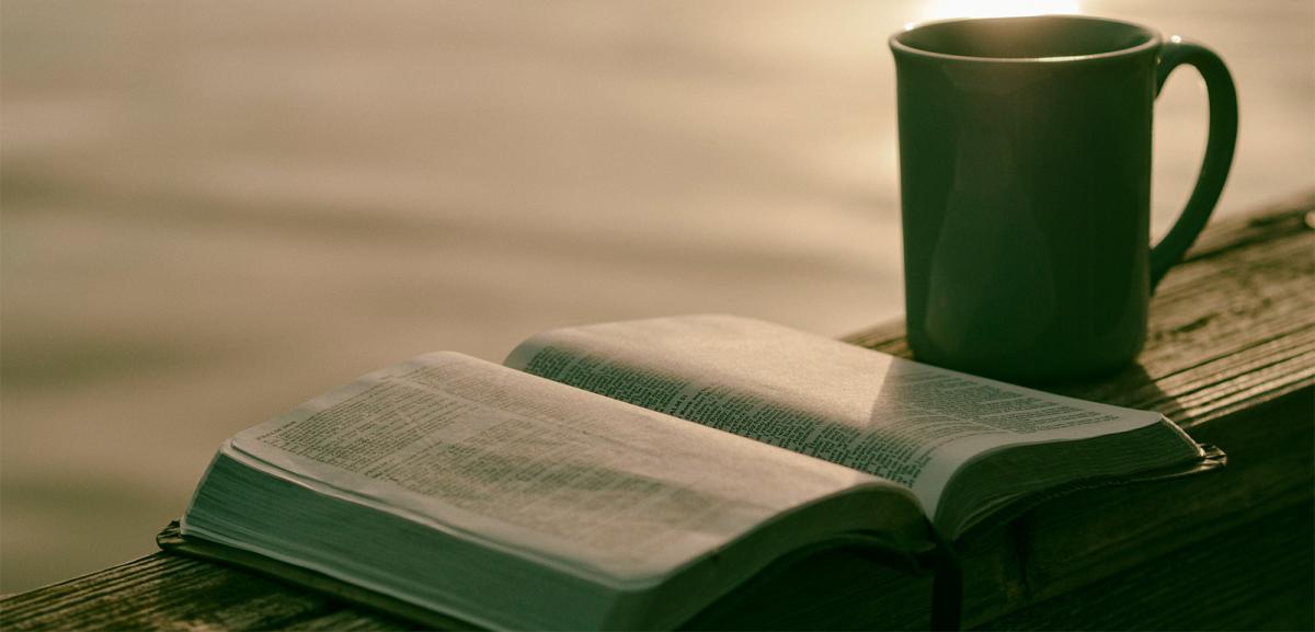 An open bible and a coffee mug with a rising sun in the background