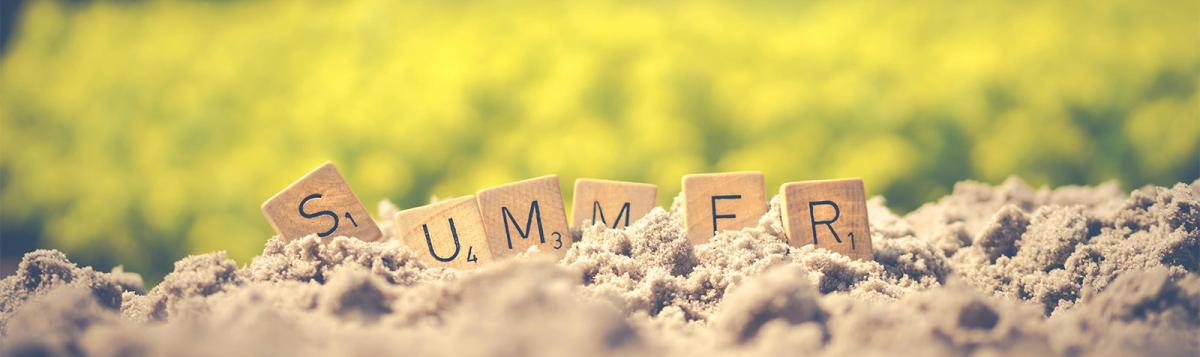 A sunny day with green grass and sand with the word summer spelled in Scrabble tiles